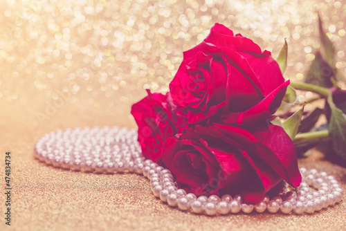 Red rose and pearl necklace on a shiny gold background

