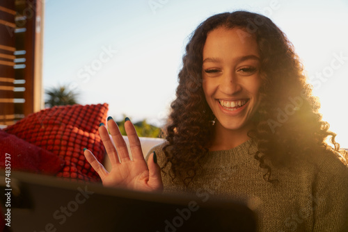 African American female waving at digital tablet while on video call with friends  photo