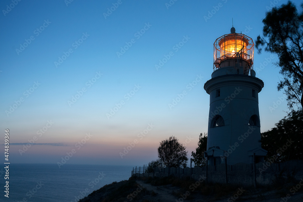 Lighthouse with a glowing lamp on a hill above the sea