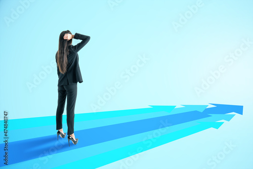 Attractive young european businesswoman with blue arrows on light background with mock up place. Way, direction and success concept.