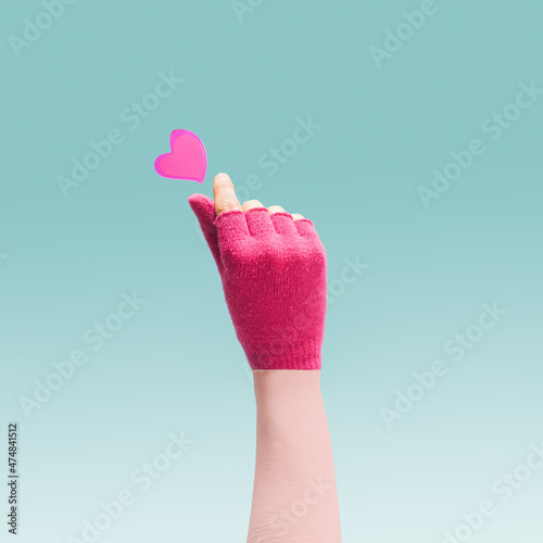 K pop concept. A girl teenager hand with magenta glove showing finger heart gesture. Red heart above. Unique blue background.