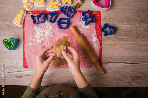 Cooking gingerbread, Christmas cookies. A rolling pin and bakeware lie on the table with gingerbread dough. The child's hands are holding a gingerbread in the shape of a heart.