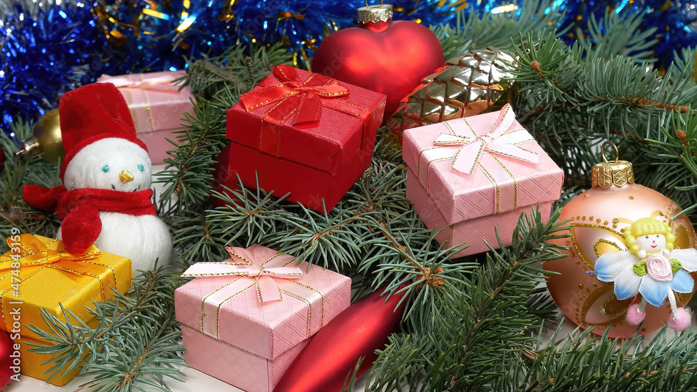 5 Christmas gifts in pink, yellow and red, along with Christmas decorations, a snowman, and a bauble fairy, in a pile of pine branches.