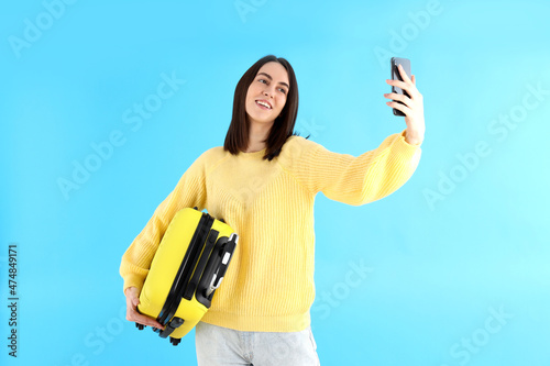 Woman with travel bag doing selfie on blue background