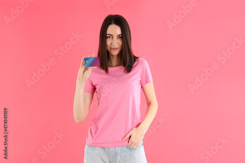 Attractive woman in t-shirt holds card on pink background