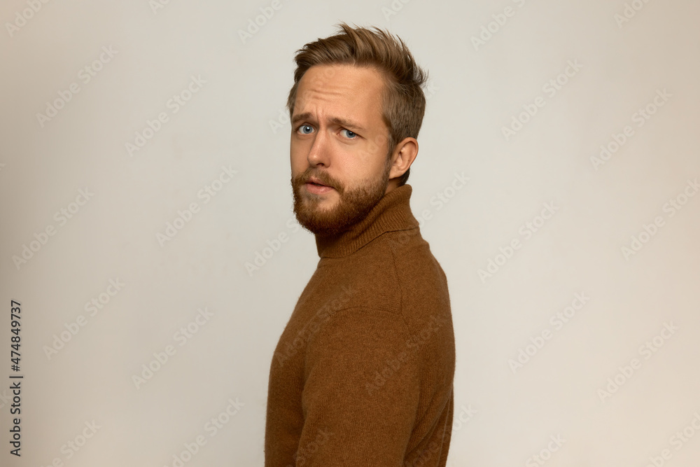 Obraz premium Picture of young brutal manful handsome blond unshaved man turned by his name looking at camera with questioning face expression, frowning with confusion, having stylish haircut and beard