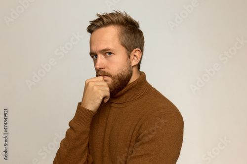 Portrait of good-looking, attractive brutal man with blond fashionable haircut, beautiful blue eyes, bearded face, holding hand under chin, planning, contemplating, frowning with thinking process © Anatoliy Karlyuk