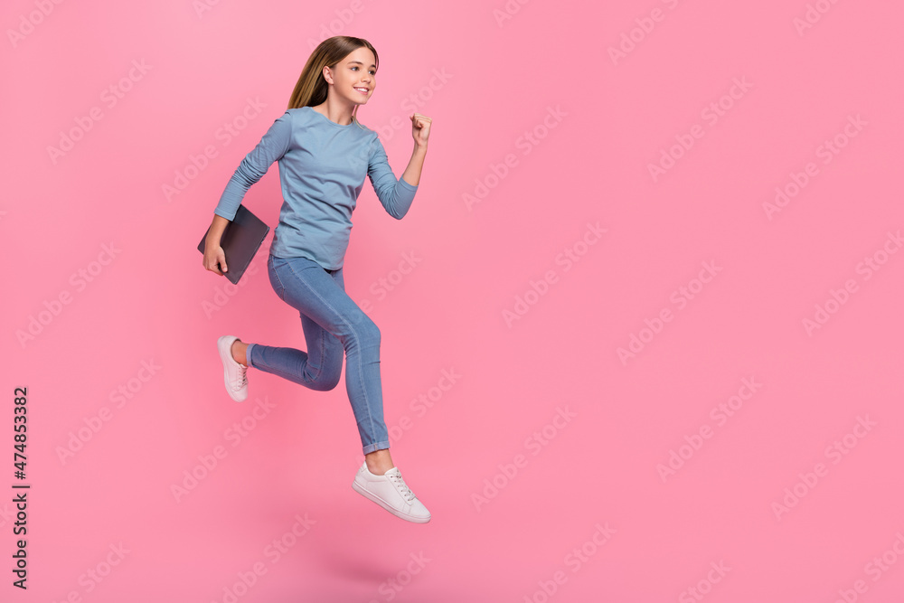 Full size profile side photo of young girl jump runner fast look empty space hold laptop courses isolated over pink color background