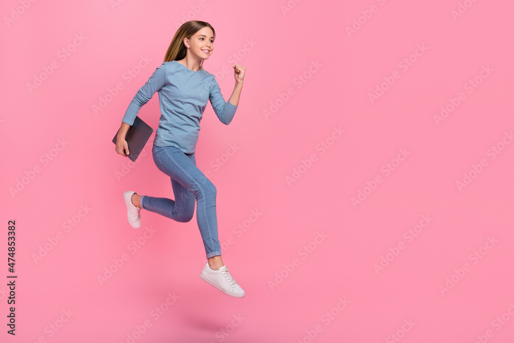Full size profile side photo of young girl jump runner fast look empty space hold laptop courses isolated over pink color background Full size profile side photo of young girl jump runner fast look empty space hold laptop courses isolated over pink color background
