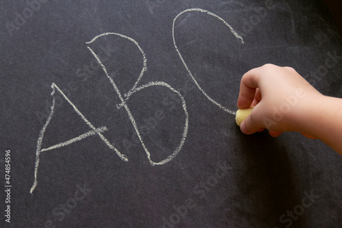 A schoolboy is learning the alphabet. School lesson. A child writes with chalk on a blackboard