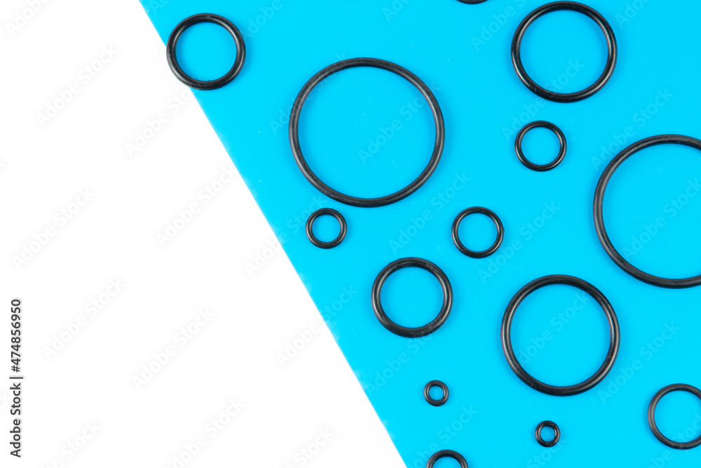 Black hydraulic and pneumatic o-rings in different sizes on a blue and white background. Rubber rings. Sealing gaskets for hydraulic connections. Rubber sealing rings for plumbing. View from above