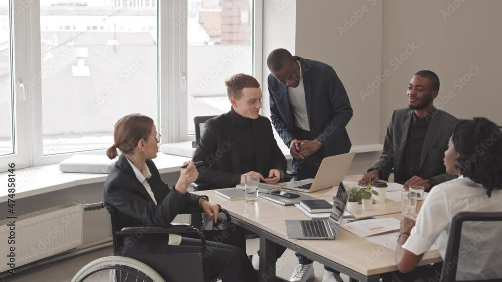 Tilting up of diverse business women and men sitting at conference table in office at daytime, having conversation on department meeting, working on project Tilting up of diverse business women and men sitting at conference table in office at daytime, having conversation on department meeting, working on project