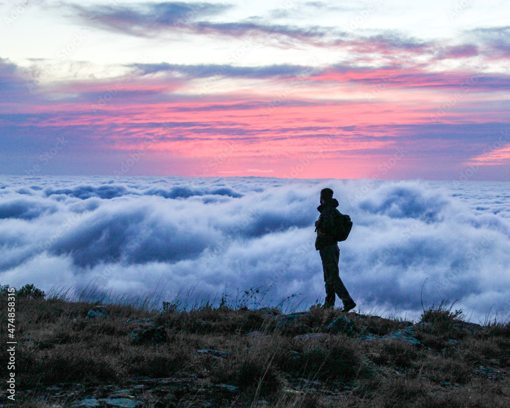 silhueta de homem com mochila nas costas caminhando na montanha ao amanhecer com mar de nuvens ao fundo