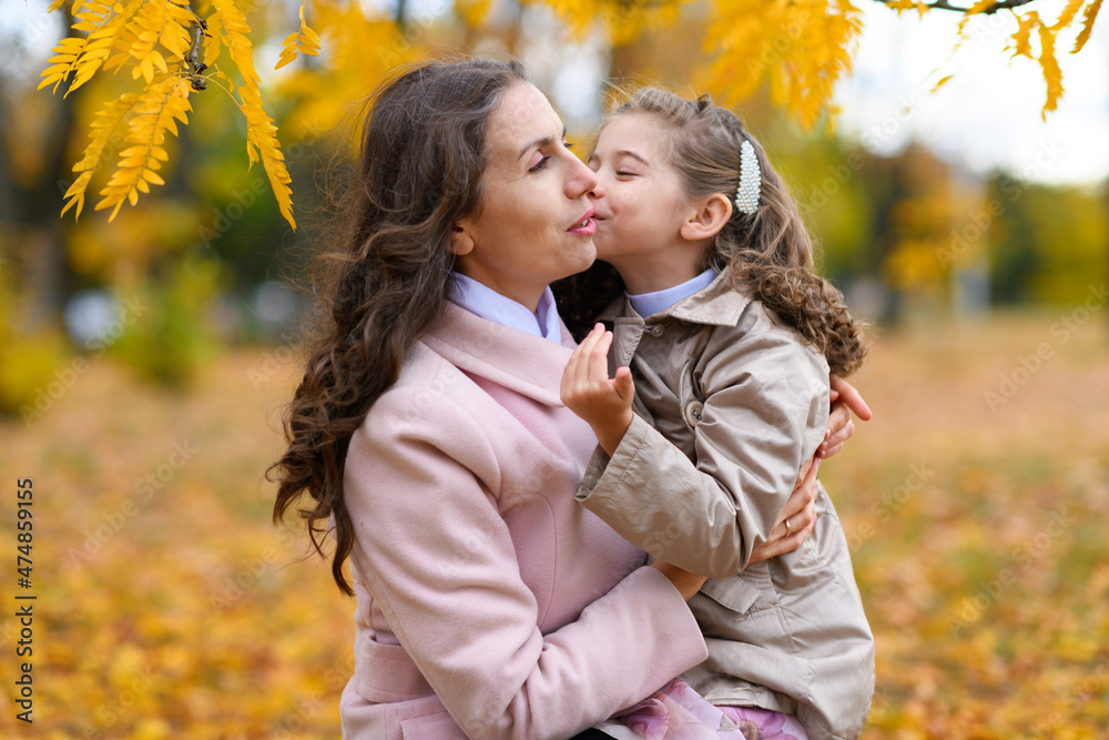 Mother and daughter portrait in an autumn park. Happy people pose against the background of beautiful yellow trees. They hug and are happy together. Mother and daughter portrait in an autumn park. Happy people pose against the background of beautiful yellow trees. They hug and are happy together.