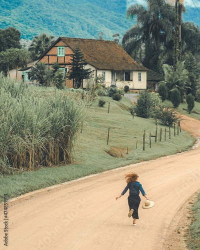 mulher correndo em estrada rural com casa enxaimel ao fundo, em Pomerode, Santa Catarina photo