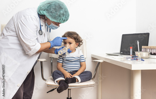 Paediatrician administers aerosolised medication while checking pneumonia in a blond Caucasian boy in a clinic.