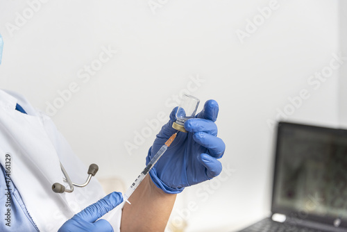 hands of a doctor preparing a syringe to inject the vaccine for immunization to covid-19 in a patient sitting in the medical consultation. Vaccination for covid-19 concept.
