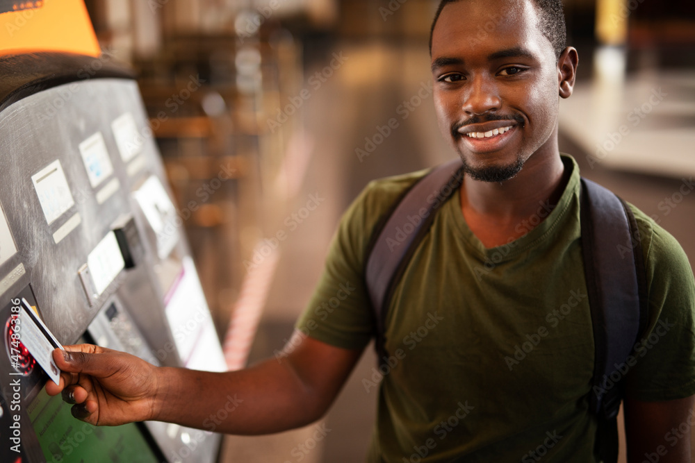 Smiling African man using ATM machine. Happy young  man withdrawing money from credit card at ATM