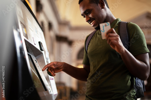 Smiling African man using ATM machine. Happy young  man withdrawing money from credit card at ATM