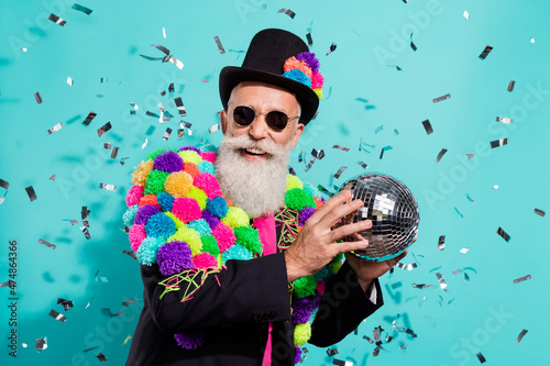 Photo of shiny funky mature showman dressed handmade pom-pom jacket holding disco ball isolated turquoise color background
