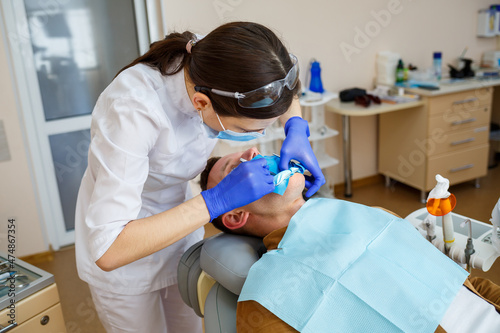 Woman dentist examines the patient with instruments in the dental clinic. The doctor makes dental treatment on the teeth of a person in the dentist's chair. Selective focus