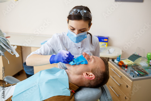 Woman dentist examines the patient with instruments in the dental clinic. The doctor makes dental treatment on the teeth of a person in the dentist s chair. Selective focus
