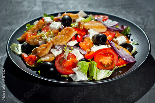 Salad with tomatoes, peppers, olives and chicken fillet. Fresh salad in a black plate on a dark background.