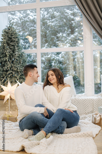 Handsome boy with his beautiful girlfriend hug each other at home at Christmas eve. Fit tree and snow outsif. Christmas mood © Aleksandr