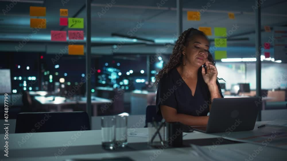 Overworked African American Businesswoman Working on Laptop Computer in Big City Office Late in the Evening. Tired Stressed Female Entrepreneur trying to Find Solution for Business Problems.