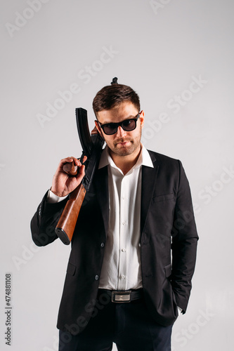 A young guy in a black suit with a gun in his hands on a white background in the studio, he depicts a security guard, bodyguard or Agent