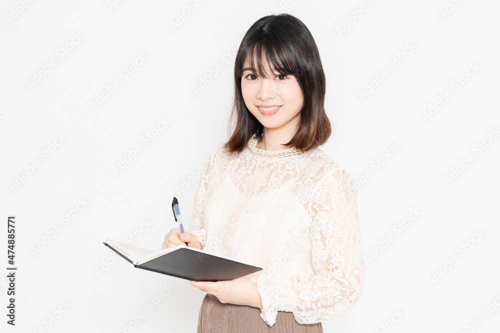白い背景の前に立って、ノートとボールペンを持っている若い女性 白い背景の前に立って、ノートとボールペンを持っている若い女性