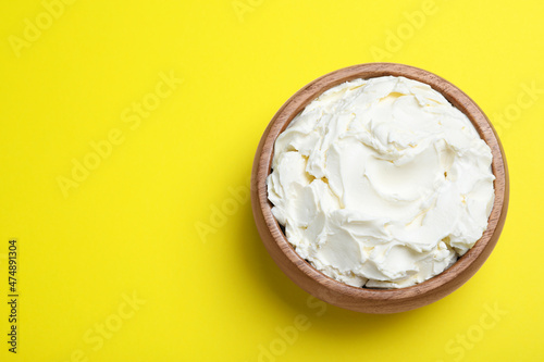 Bowl of tasty cream cheese on yellow background, top view. Space for text