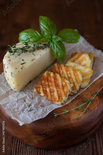 Slices of fried halloumi cheese with a beautiful grilling pattern rests on a wooden tray.