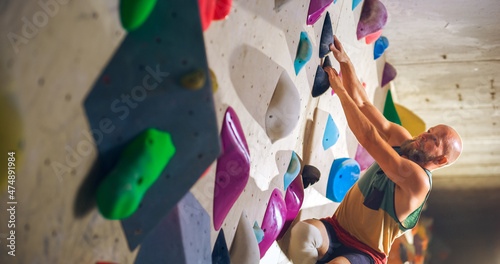 Strong Experienced Rock Climber Practicing Solo Climbing on Bouldering Wall in Gym. Man Exercising at Indoor Fitness Facility, Doing Extreme Sport for His Healthy Lifestyle Training. Close Up Portrait