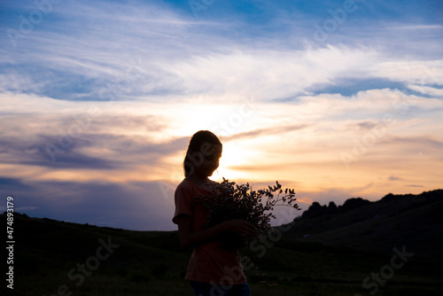 Silhouette of a girl with a bouquet of flowers on the background of a sunset in the mountains. The concept of summer fun