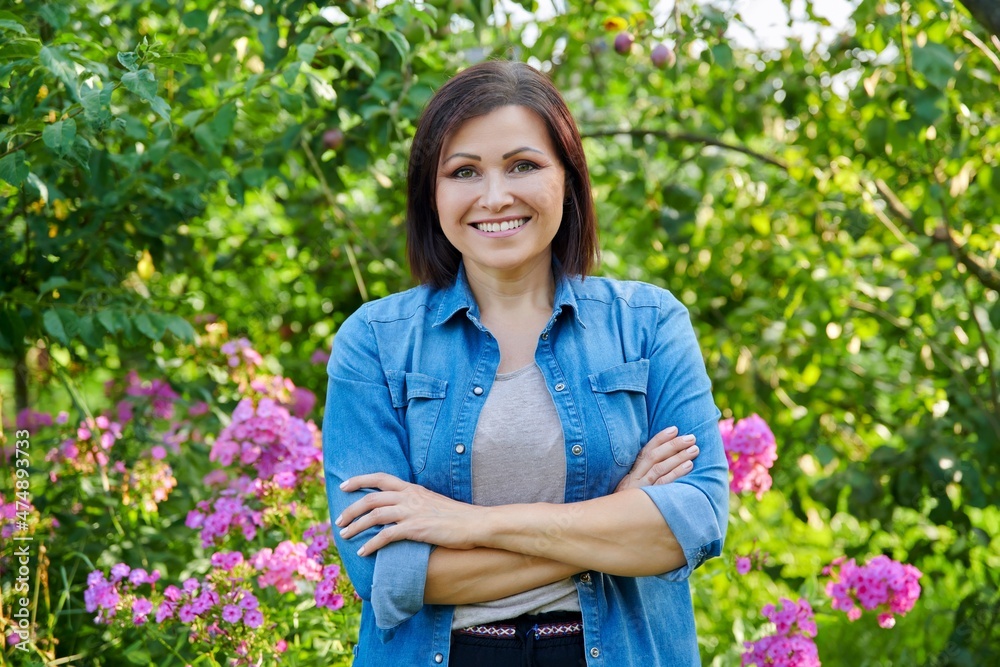 Portrait of smiling confident middle aged woman with crossed arms in garden Portrait of smiling confident middle aged woman with crossed arms in garden