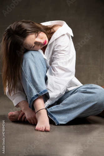 A girl in a white shirt and jeans sits with her head on her knees. Sad girl. © Светлана Лазаренко