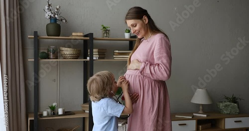 Cute little boy play doctor with smiling mother expecting child. Son preschooler move stethoscope by belly of pregnant mom tickle stroke tummy of mum try to hear unborn baby heartbeat movements inside photo