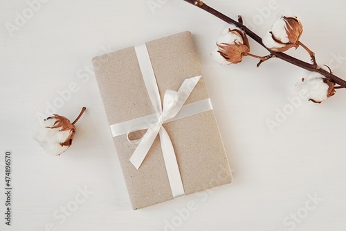 Valokuva Gift box mockup wrapped with brown paper and white ribbon, cotton branches as decoration, space for gift label or sticker presentation