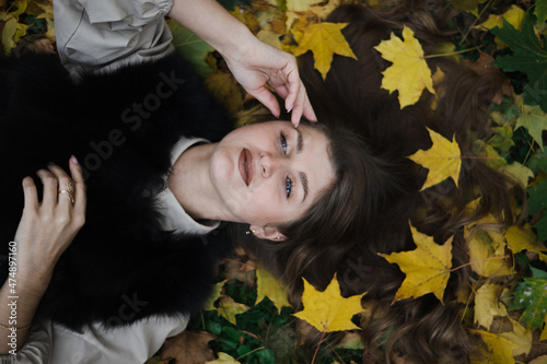 beautiful pose in autumn leaves. the girl lies on yellow leaves. leaves adorn the hair. blue eyes look up to the sky. the girl touches her face with her hand.