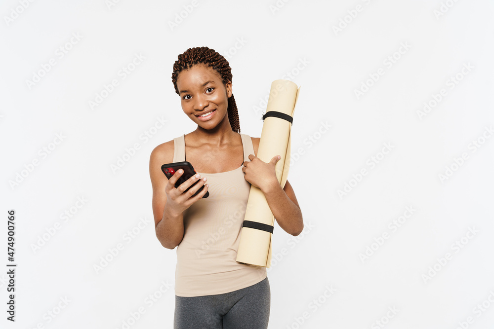 Young black woman using cellphone while posing with fitness mat Young black woman using cellphone while posing with fitness mat