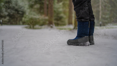 A teenager in winter blue boots stands on the white snow on a flattering path.