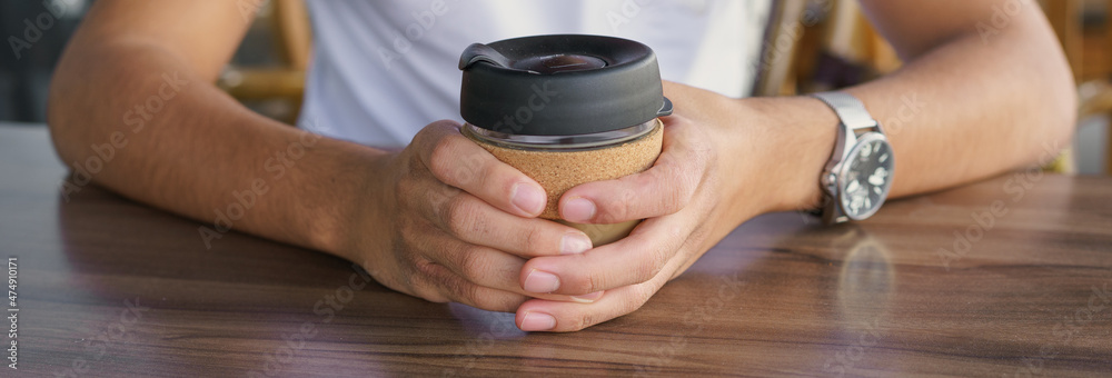 Banner male hands hold reusable coffee mug. Young man drink coffee from reusable travel coffee cup. Teenager holding reusable coffee mug. Sustainable lifestyle. Eco friendly concept.