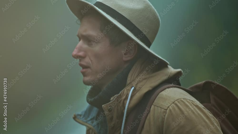close up portrait of man hitchhiker wearing in retro style. traveler in hat with backpack stands outdoors at road in cold wet foggy autumn day and waites a car. soft focus close up portrait of man hitchhiker wearing in retro style. traveler in hat with backpack stands outdoors at road in cold wet foggy autumn day and waites a car. soft focus