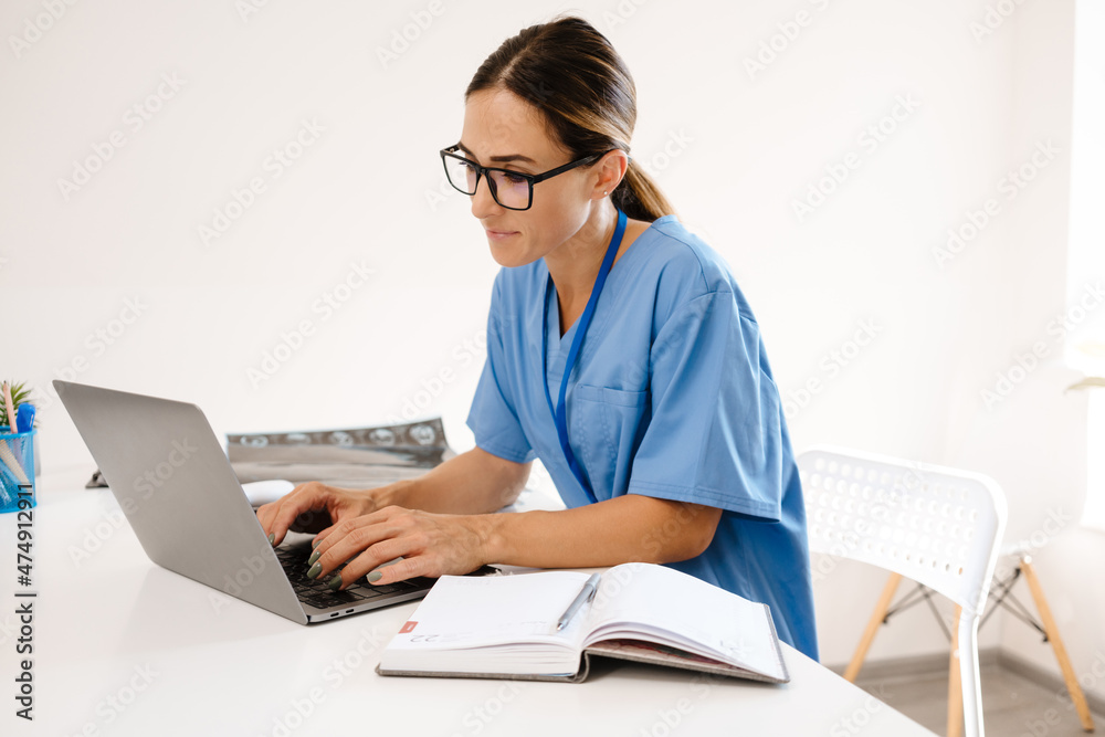 White woman doctor typing on laptop while working in office White woman doctor typing on laptop while working in office