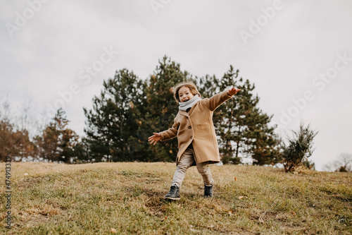 Little boy running, smiling, spending time outdoors in a park on autumn day.