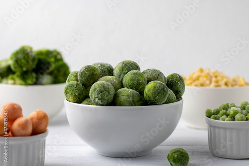 Bowls of frozen vegetables: Brussels sprouts, peas, broccoli, corn, peas, carrots on a white plate. Side view, horizontal composition