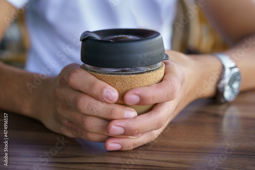 Male hands hold reusable coffee mug. Young man drink coffee from reusable travel coffee cup. Teenager holding reusable coffee mug. Sustainable lifestyle. Eco friendly concept.