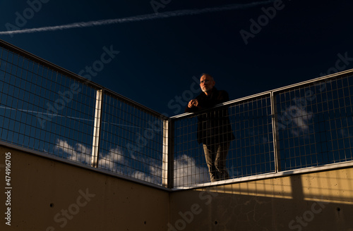 Adult man standing against fence with blue cloudy sky during sunset