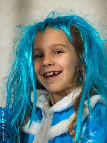 A smiling school-age girl in a blue wig and snow maiden costume against a gray background. Close-up of a happy child's face. photo